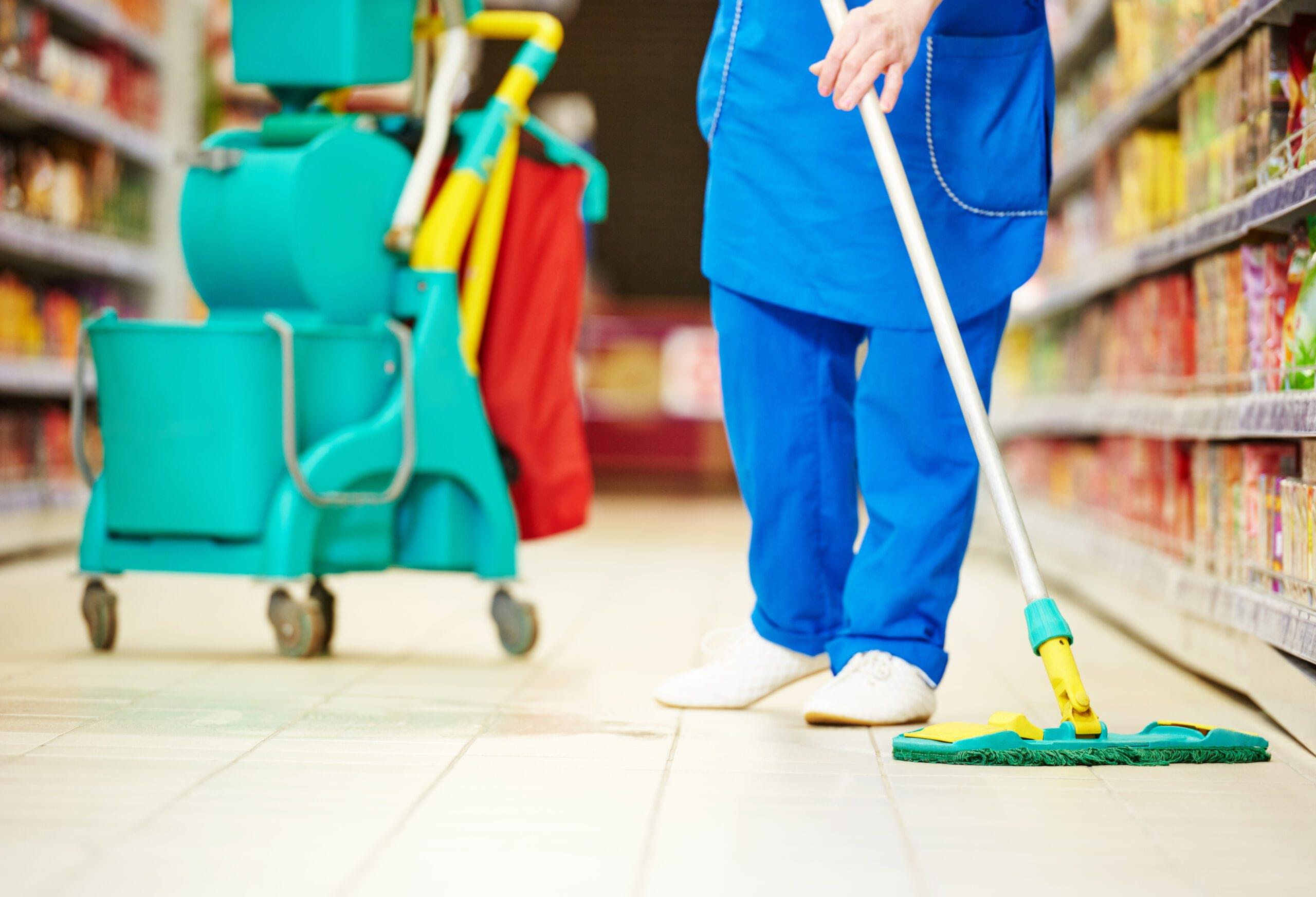 Female cleaner worker in uniform with mop cleaning the floor of supermarket shop store