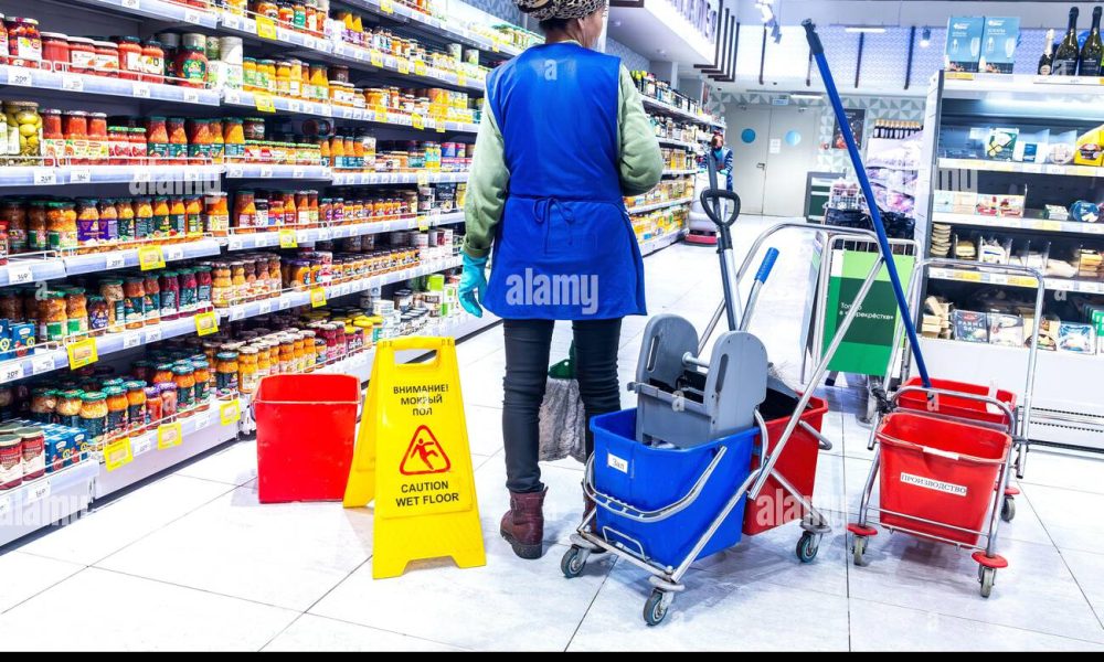 samara-russia-may-9-2025-cleaning-service-workers-wash-the-floor-in-a-supermarkets-sales-area-caution-wet-floor-warning-sign-on-a-tile-floor-in-3E56ATW